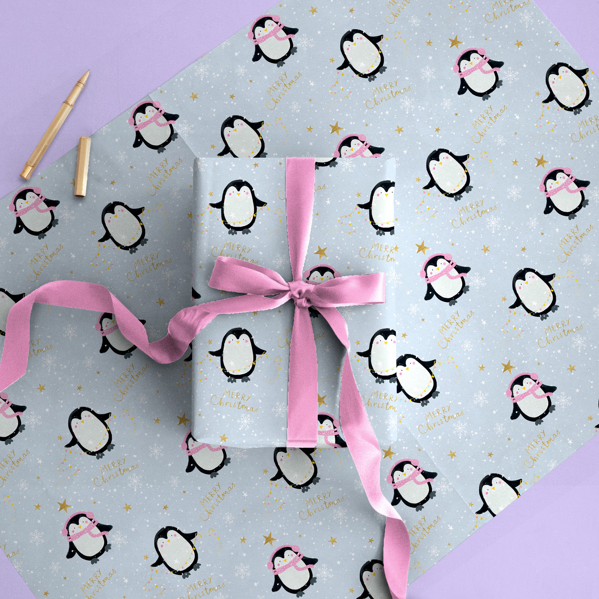 Penguins Christmas wrapping paper featuring cute penguins, gold stars, and Merry Christmas text on a light blue background.