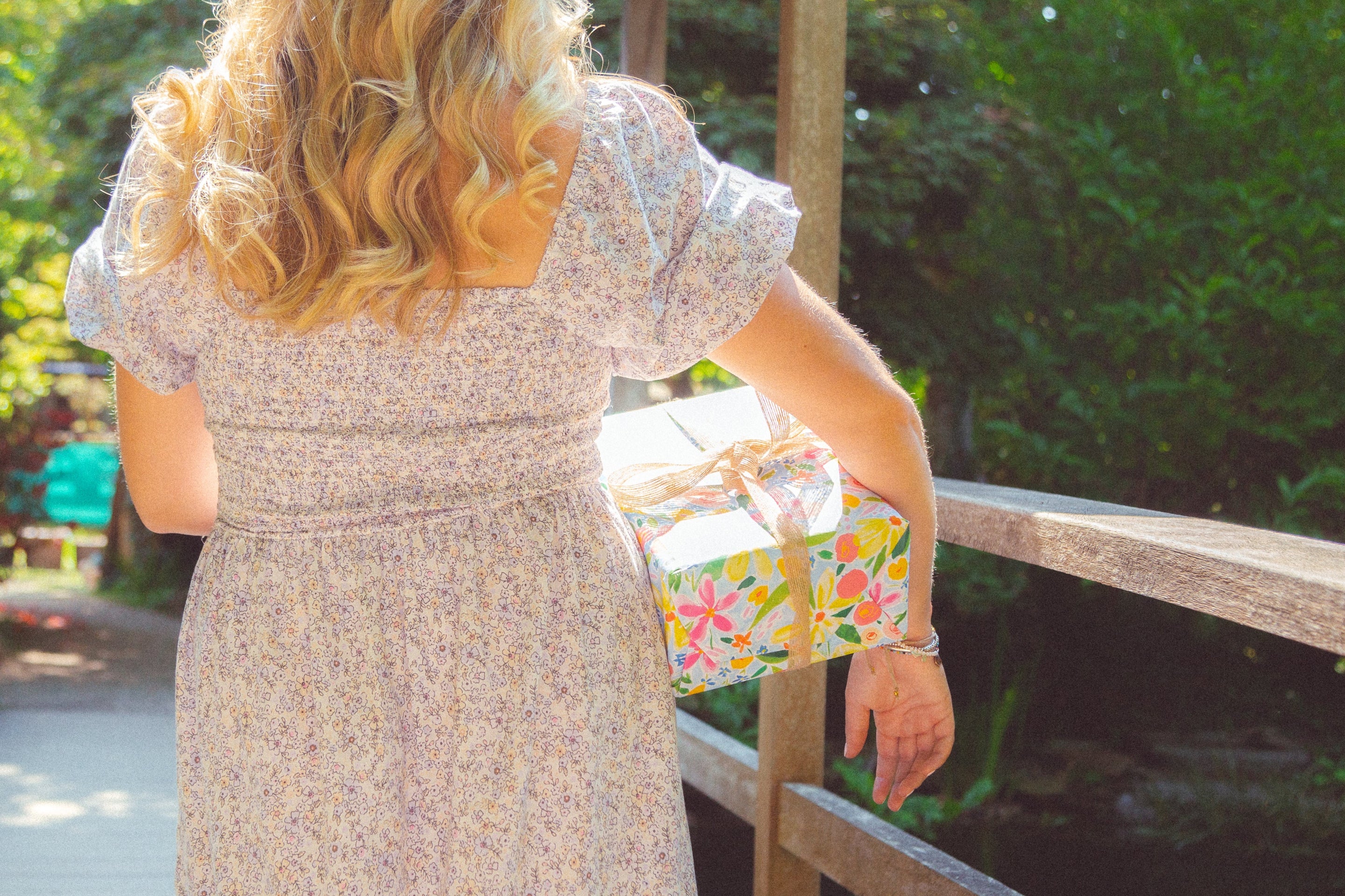 A present covered in bright floral wrapping paper and a hessian bow being carried by a women in a dress