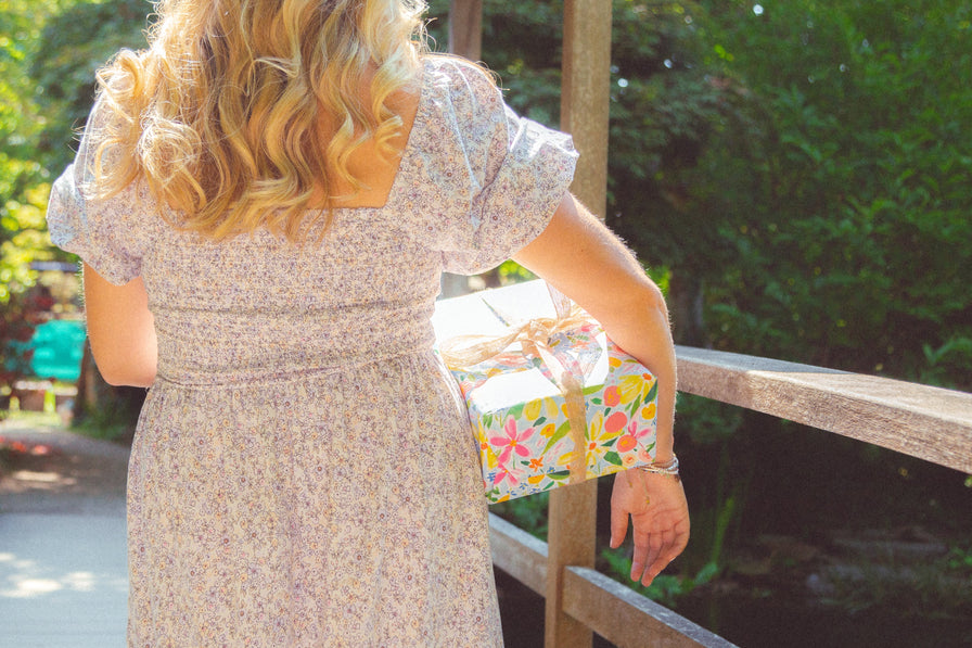 A present covered in bright floral wrapping paper and a hessian bow being carried by a women in a dress