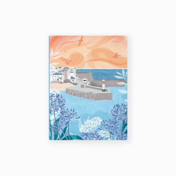 St Ives notebook featuring a coastal harbour scene with blue flowers, a lighthouse, and a soft orange sunset sky.