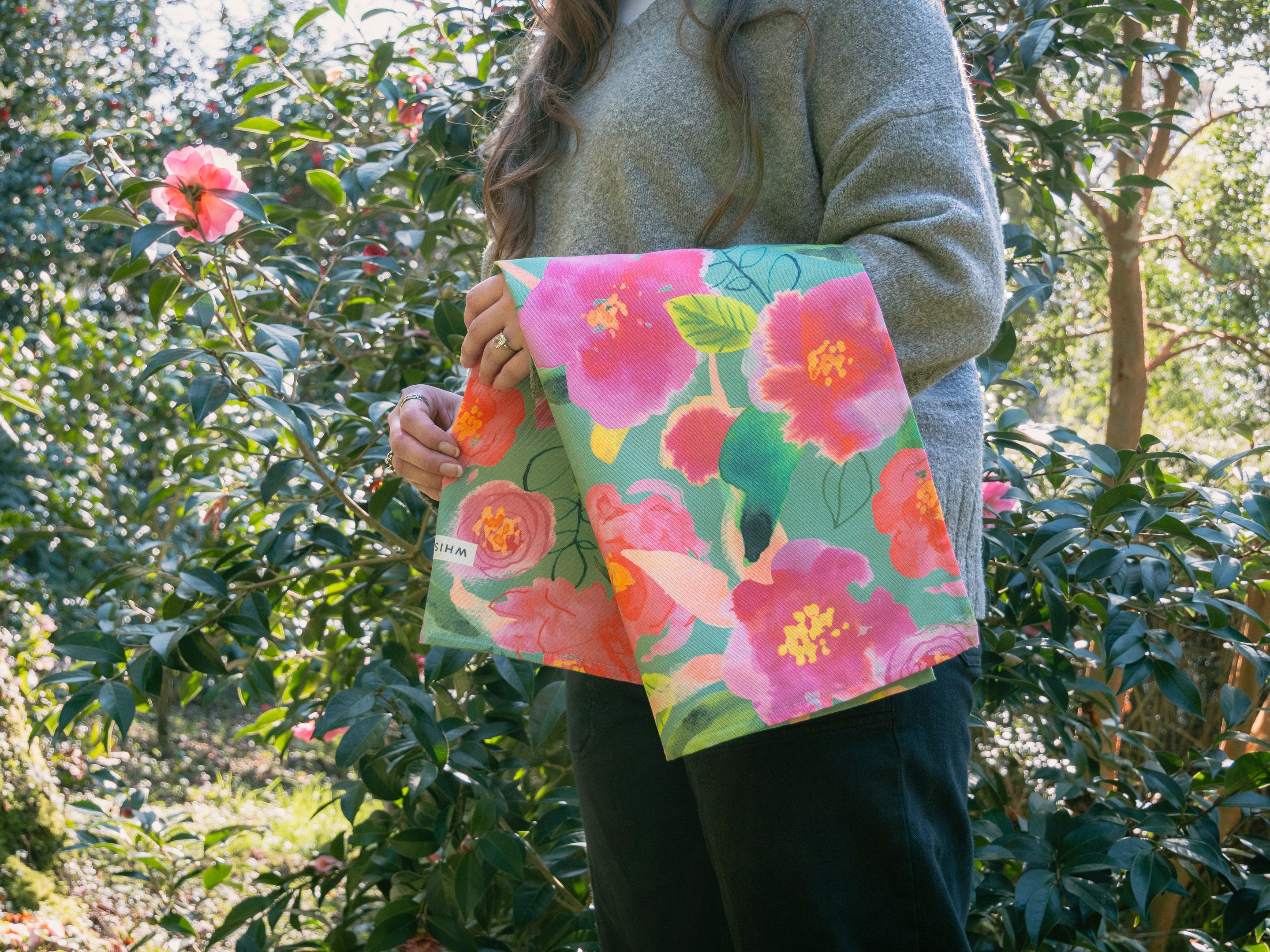 A tea towel over a womans arm in a garden by a camellia tree