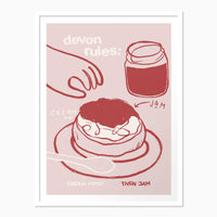 Devon Rules framed print featuring a pink illustration of a scone with cream and jam, set in a simple white frame.