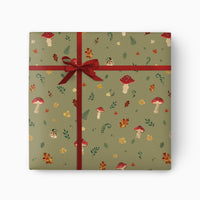 Wild Mushrooms wrapping paper in sage green with red toadstools, autumn leaves, and a tied dark red ribbon bow.