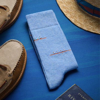 The Regatta Blue socks in a light blue shade featuring a small rowing boat pattern, displayed with tan suede boat shoes.