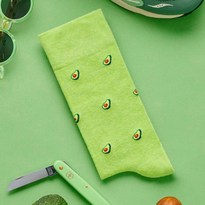 Light green socks featuring a small avocado pattern, displayed on a matching green background.