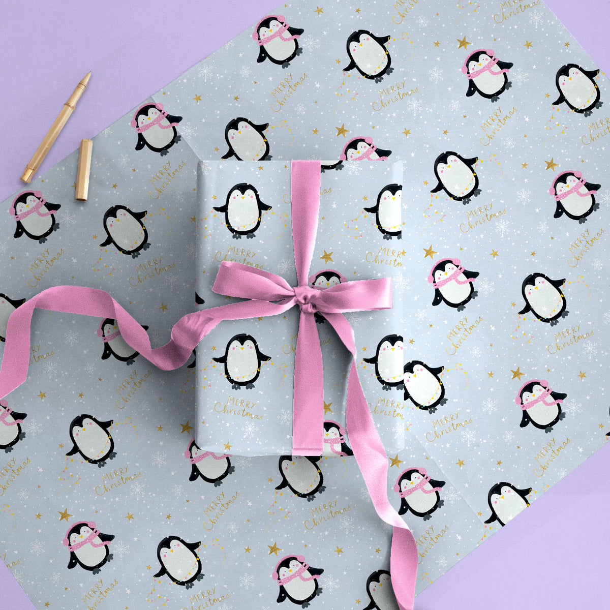 Penguins Christmas wrapping paper featuring cute penguins, gold stars, and Merry Christmas text on a light blue background.