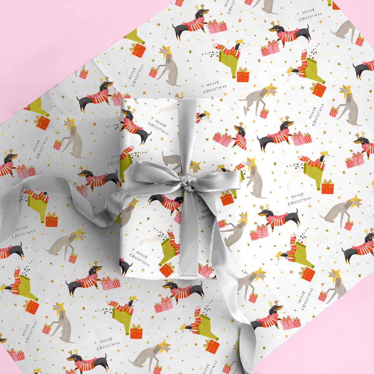 Party Pups Christmas wrapping paper featuring illustrated dogs in festive jumpers and gifts with gold stars on white.