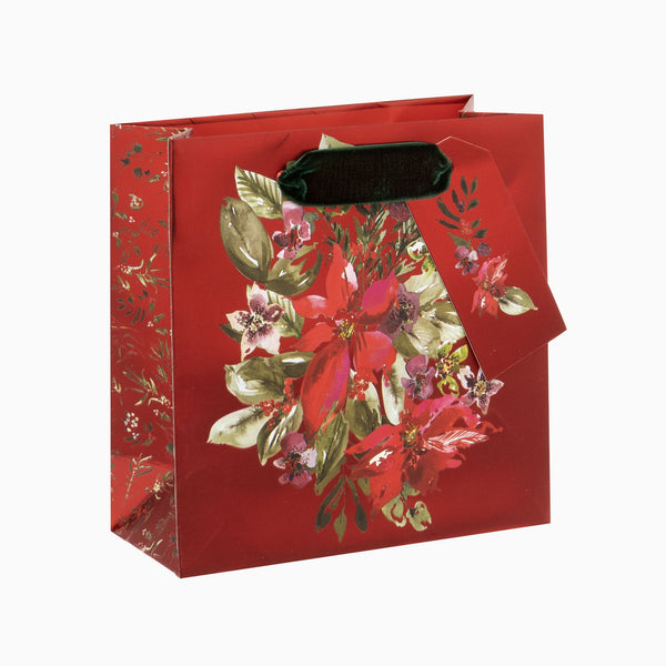 Small red gift bag featuring a festive poinsettia floral design with a dark green velvet handle and matching gift tag.