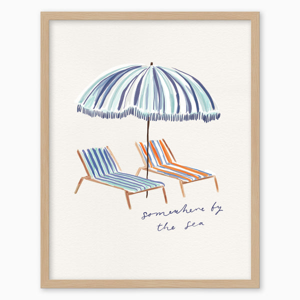 Somewhere by the Sea framed print featuring a blue striped parasol and two colourful deckchairs on a white background.