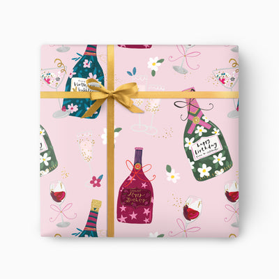 Birthday Bottles wrapping paper with a pink background, illustrated champagne bottles, wine glasses, and a gold ribbon.