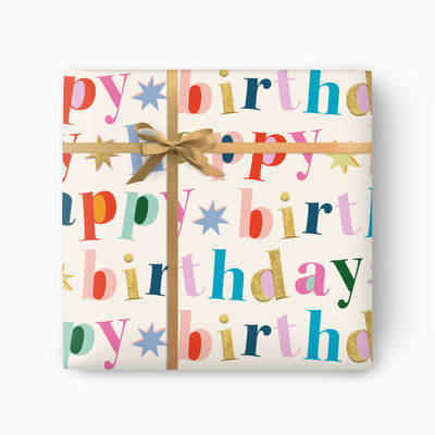 Bold Birthday wrapping paper with multicoloured Happy Birthday lettering and star icons, tied with a gold ribbon.