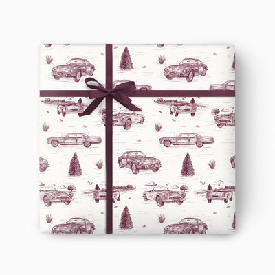 Cars Toile wrapping paper featuring a purple ink sketch pattern of vintage cars and pine trees, tied with a purple ribbon.
