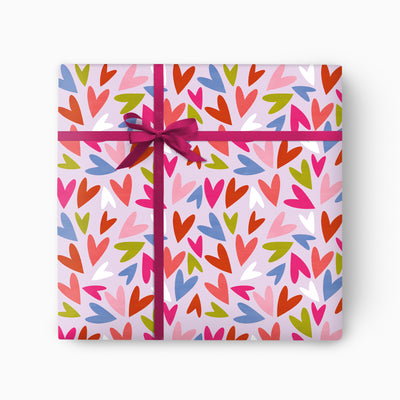 Happy Hearts wrapping paper featuring a colourful heart pattern on a pale pink background tied with a dark pink ribbon.