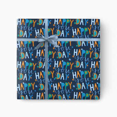 Happy You Day navy wrapping paper featuring colourful text and star patterns, tied with a light blue ribbon.