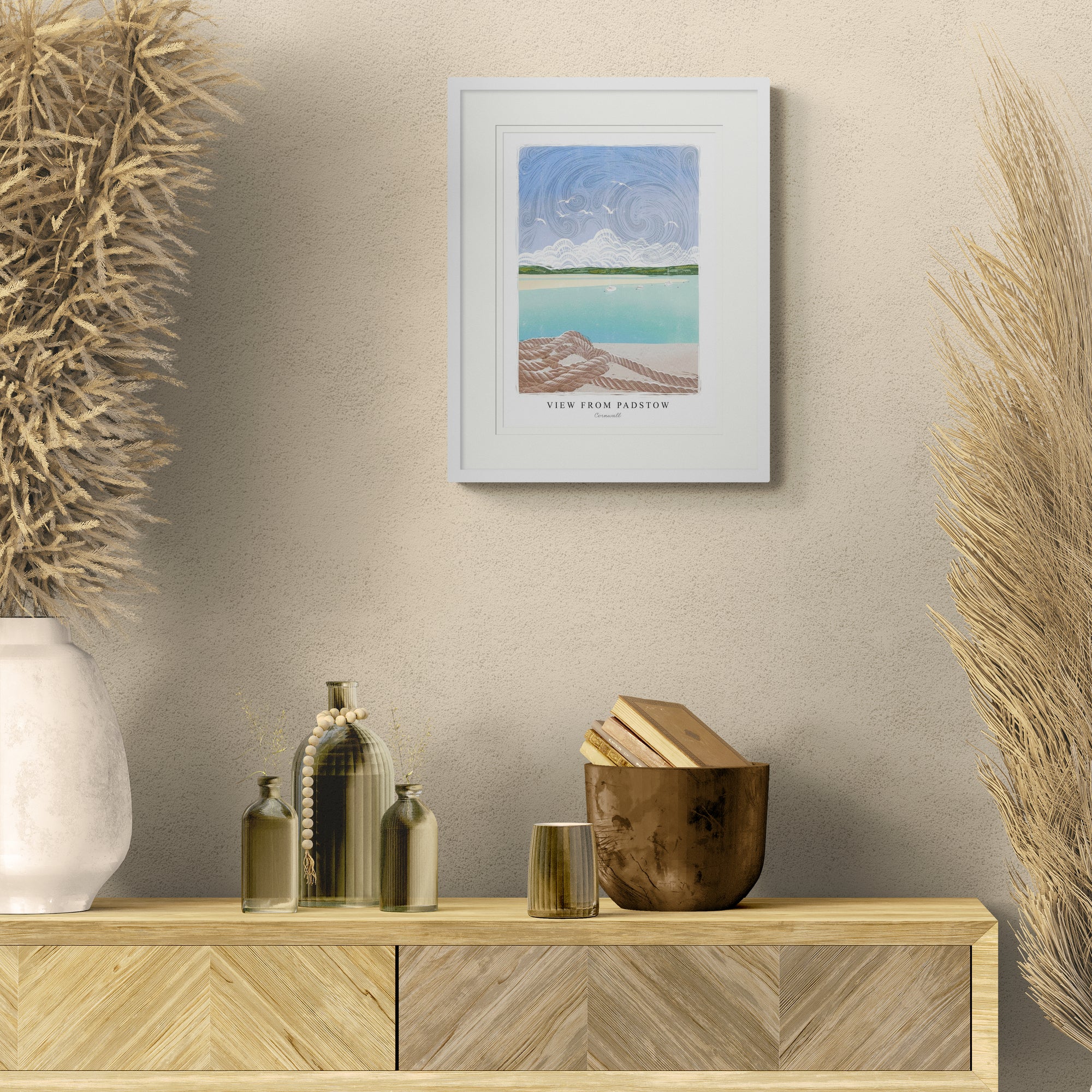 Small framed lino print of a coastal scene in Padstow, featuring a blue sky, turquoise sea, and rope in a white frame.