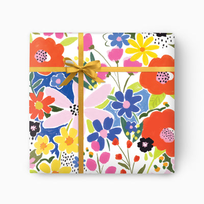 Neon Wild wrapping paper featuring a vibrant floral pattern in red, blue, yellow and pink, tied with a gold ribbon.