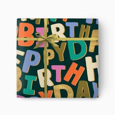 Party Letters wrapping paper featuring colourful, scattered birthday letters on a dark green background with a gold ribbon.