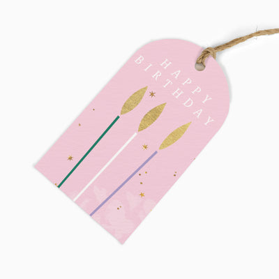 Pink Happy Birthday gift tag with three candles, gold flames, and small stars, attached to a piece of brown twine.