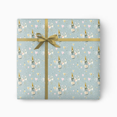 Pop & Sparkle wrapping paper featuring champagne bottles, glasses, and hearts on a pale blue background with a gold ribbon.