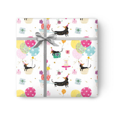 Sausage Dog Party wrapping paper featuring dachshunds in party hats, colourful balloons, gifts, and cake on white.