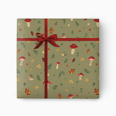 Wild Mushrooms wrapping paper in sage green with red toadstools, autumn leaves, and a tied dark red ribbon bow.