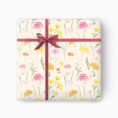 Yarrow Meadow Cream wrapping paper featuring a watercolour floral pattern in pink, yellow and green with a dark pink ribbon.
