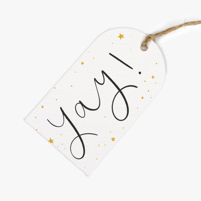 Yay! gift tag with black handwritten lettering, gold stars, and dots on a white background with brown twine string.